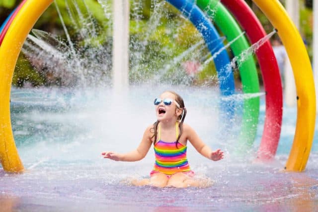 Kids play in aqua park. Children at water playground of tropical amusement park. Little girl at swimming pool. Child playing at water slide on summer vacation in Asia. Swim wear for young kid.
