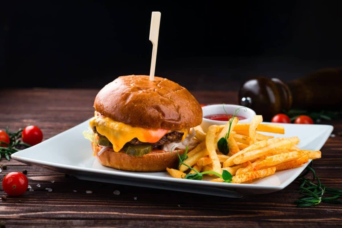 Cheeseburger with beef, tomato, pickles cucumber, red onion, lettuce, cheddar cheese, ketchup and French fries. Tasty burger cooking with beef, tomato, cheese, cucumber and lettuce.