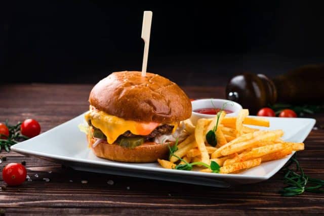 Cheeseburger with beef, tomato, pickles cucumber, red onion, lettuce, cheddar cheese, ketchup and French fries. Tasty burger cooking with beef, tomato, cheese, cucumber and lettuce.