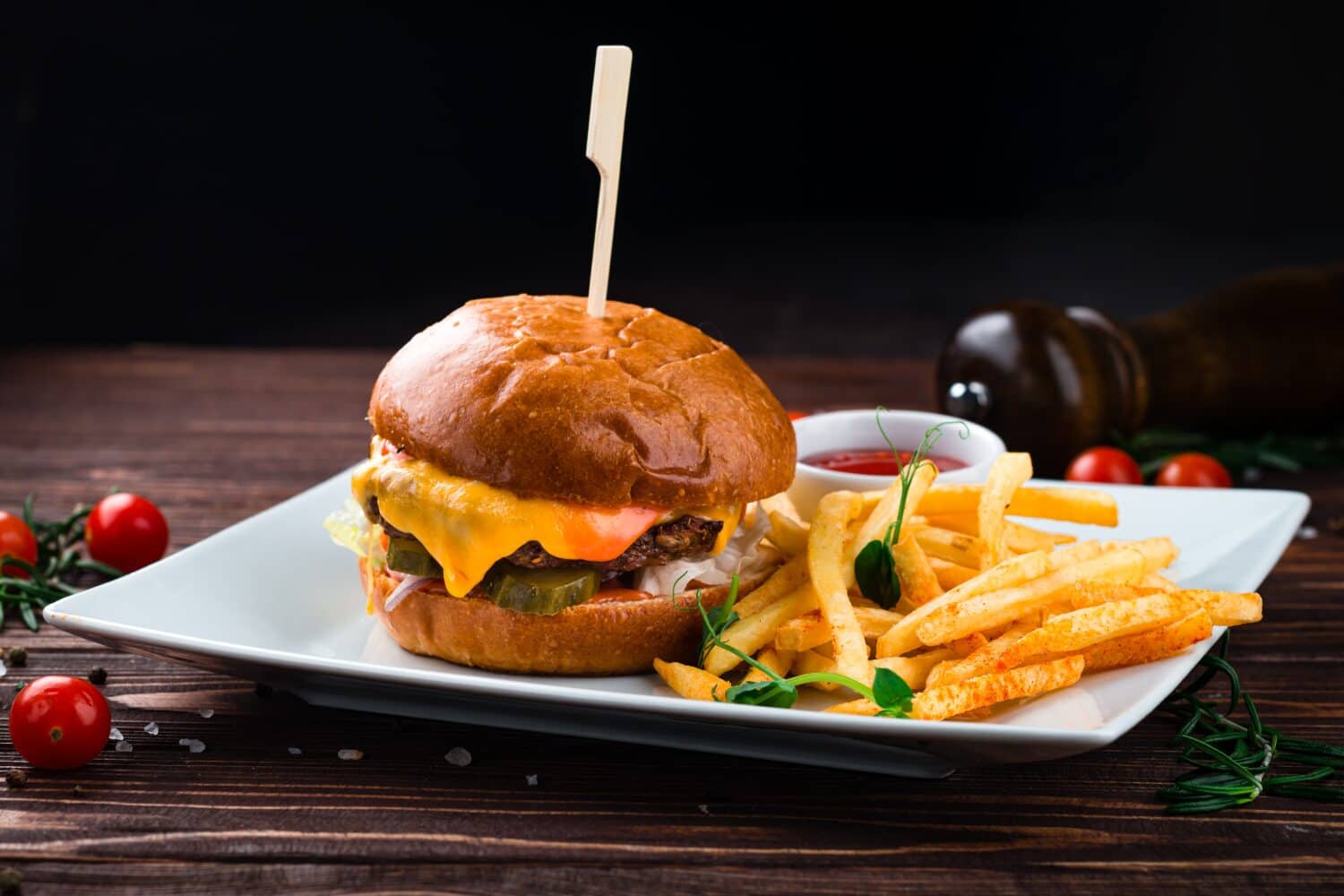 Cheeseburger with beef, tomato, pickles cucumber, red onion, lettuce, cheddar cheese, ketchup and French fries. Tasty burger cooking with beef, tomato, cheese, cucumber and lettuce.