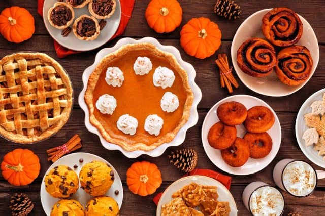 Autumn desserts table scene with an assortment of traditional fall sweet treats. Above view over a rustic wood background. Pumpkin and apple pies, apple cider donuts, muffins, cookies, tarts.