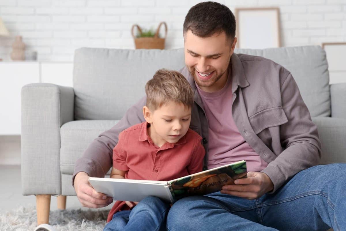 Happy father and his little son reading book together at home