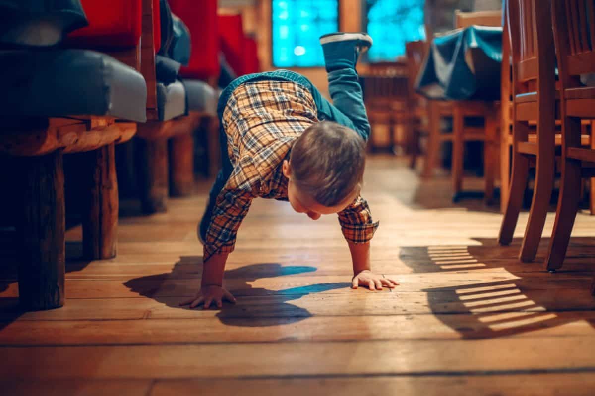 Cute adorable boy three years old having fun in cafe restaurant. Child playing on floor in public place. Freedom of self expression and behaviour for kids. Toddler touching dirty ground.