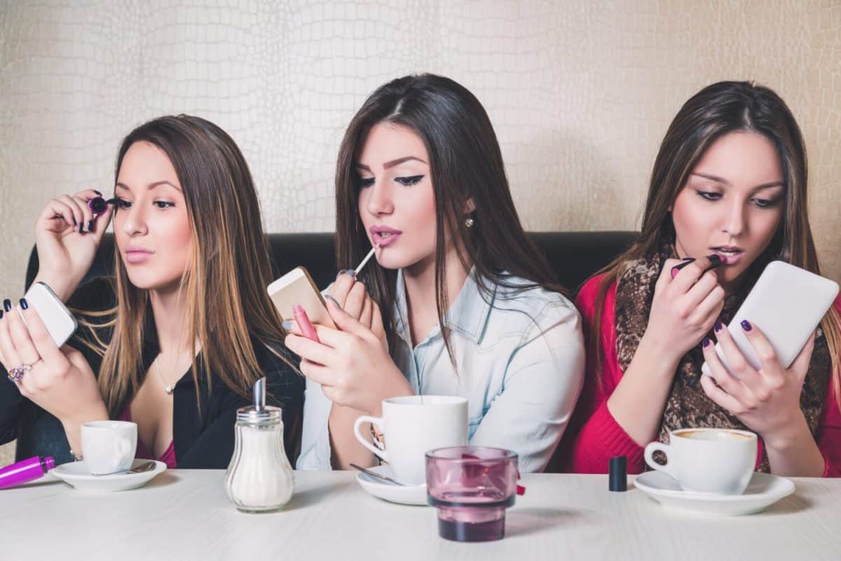 Three girls putting on makeup in a cafe
