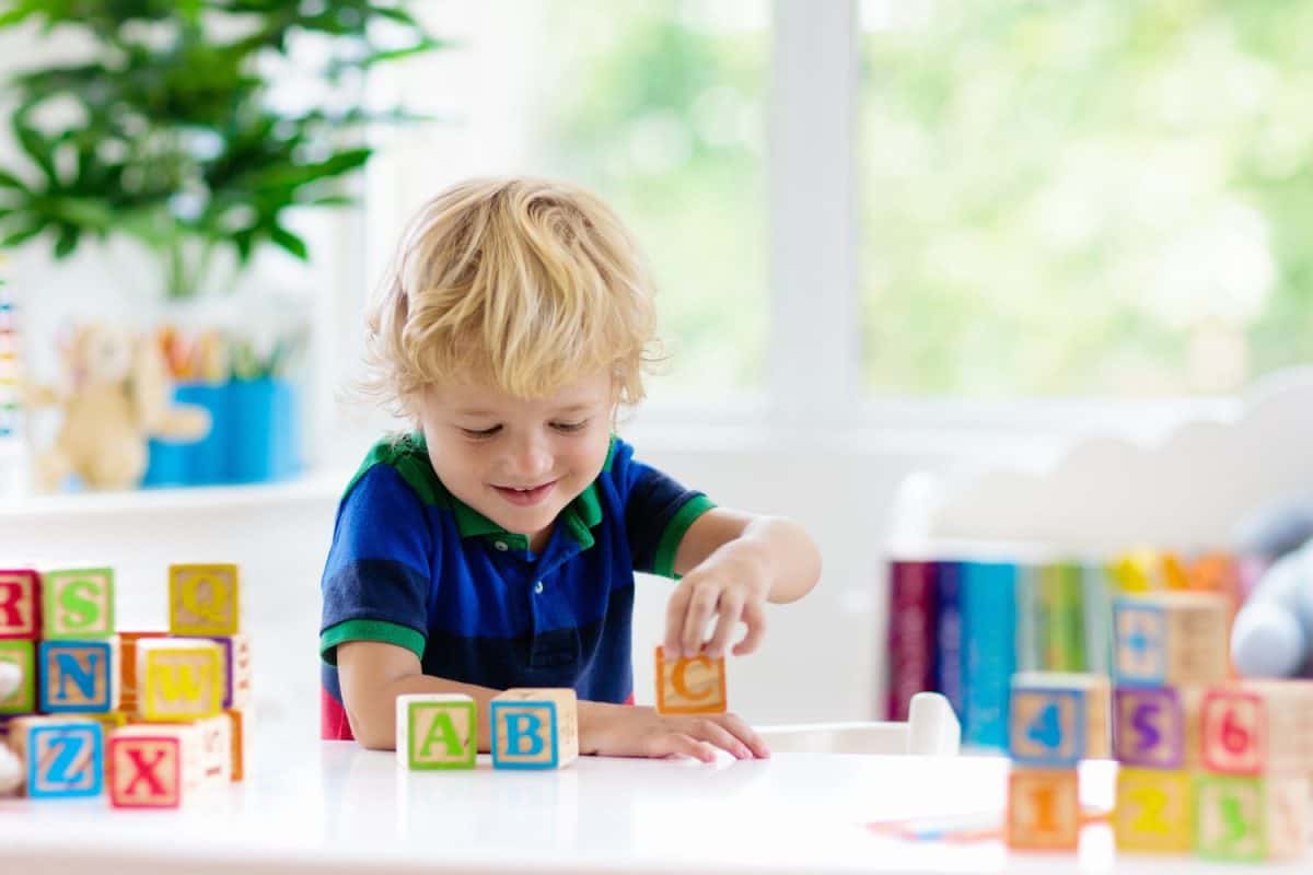 Child learning letters and numbers. Kid with colorful wooden abc blocks. Little boy spelling words with educational block toys. Kids doing school homework at white desk. Bedroom for preschool children
