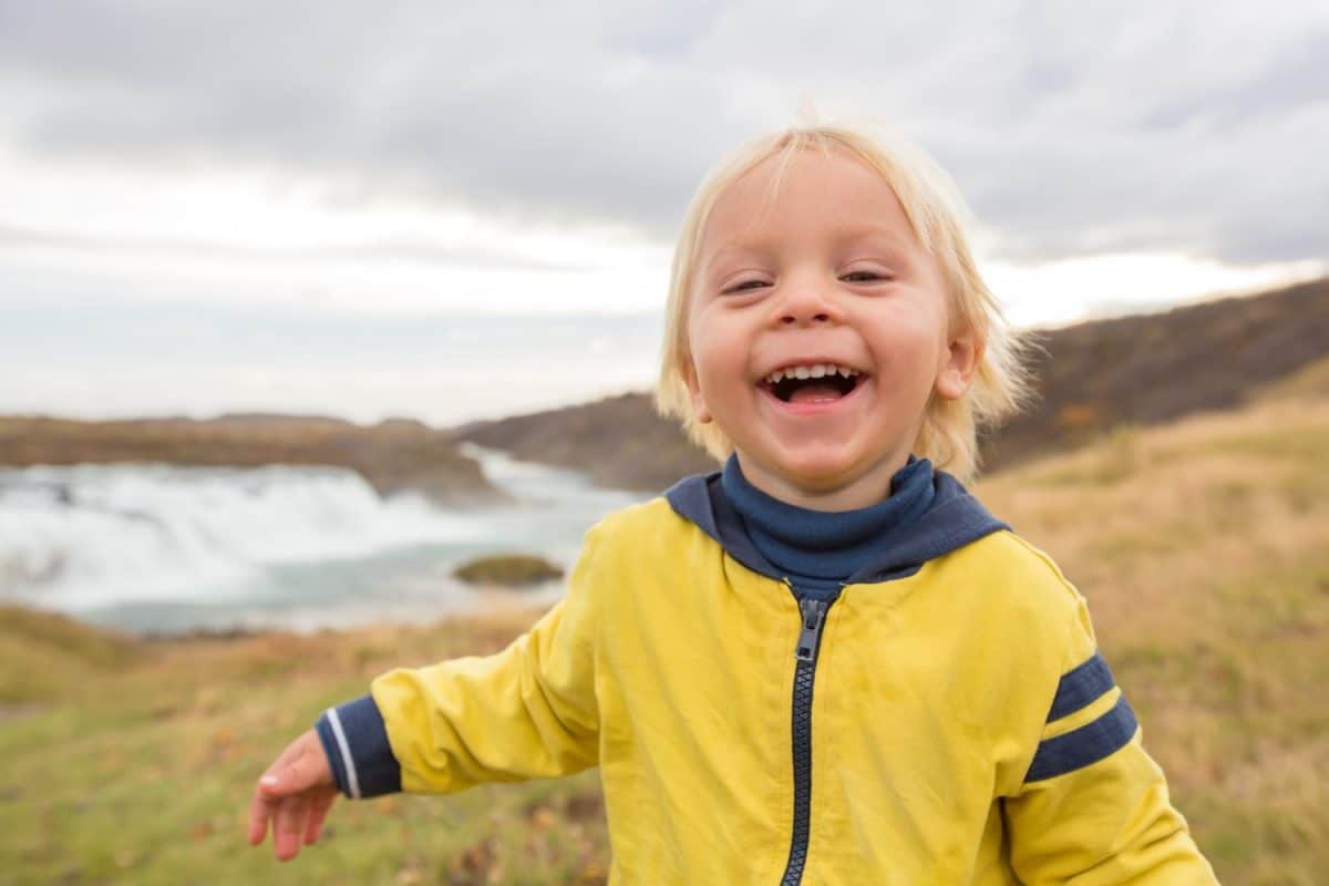 Portrait of a smiling baby boy near smaller waterfall around Gullfoss, Iceland autumntime