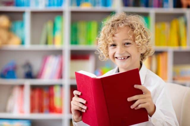 Child reading book. Kids read. Little boy at a colorful bookshelf doing homework for school. Student with books. Early education and development. Home library for children. Preschool kid study.