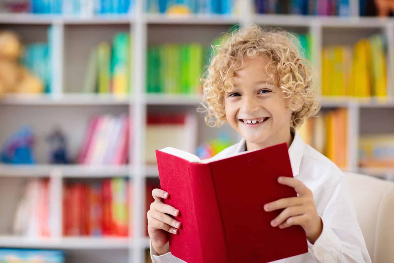 Child reading book. Kids read. Little boy at a colorful bookshelf doing homework for school. Student with books. Early education and development. Home library for children. Preschool kid study.