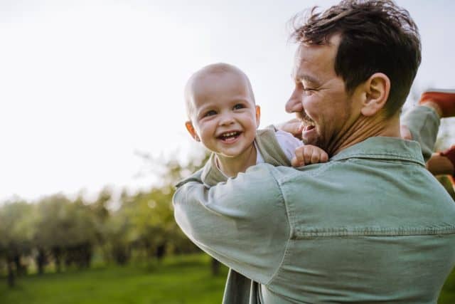 Father holding little baby, playing, having fun during warm spring day. Father's day concept.