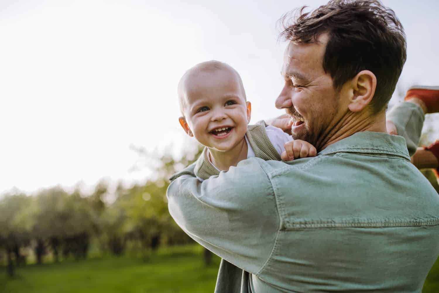 Father holding little baby, playing, having fun during warm spring day. Father's day concept.