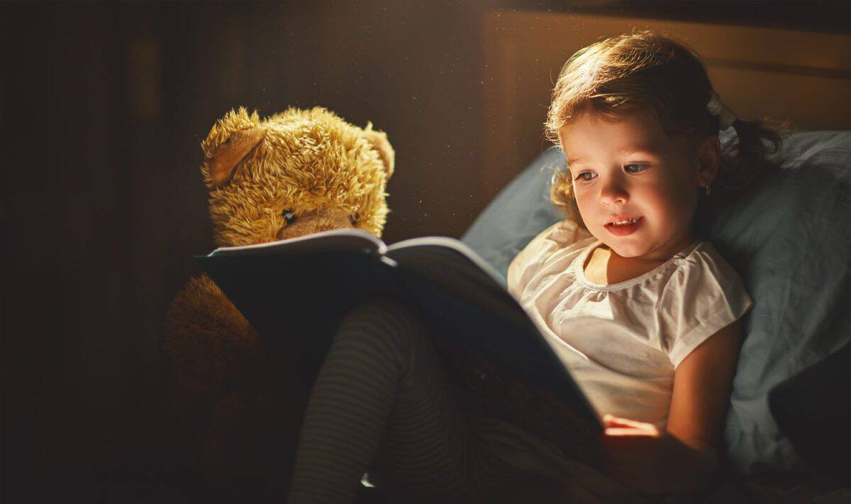 child girl reading a book in bed before going to sleep