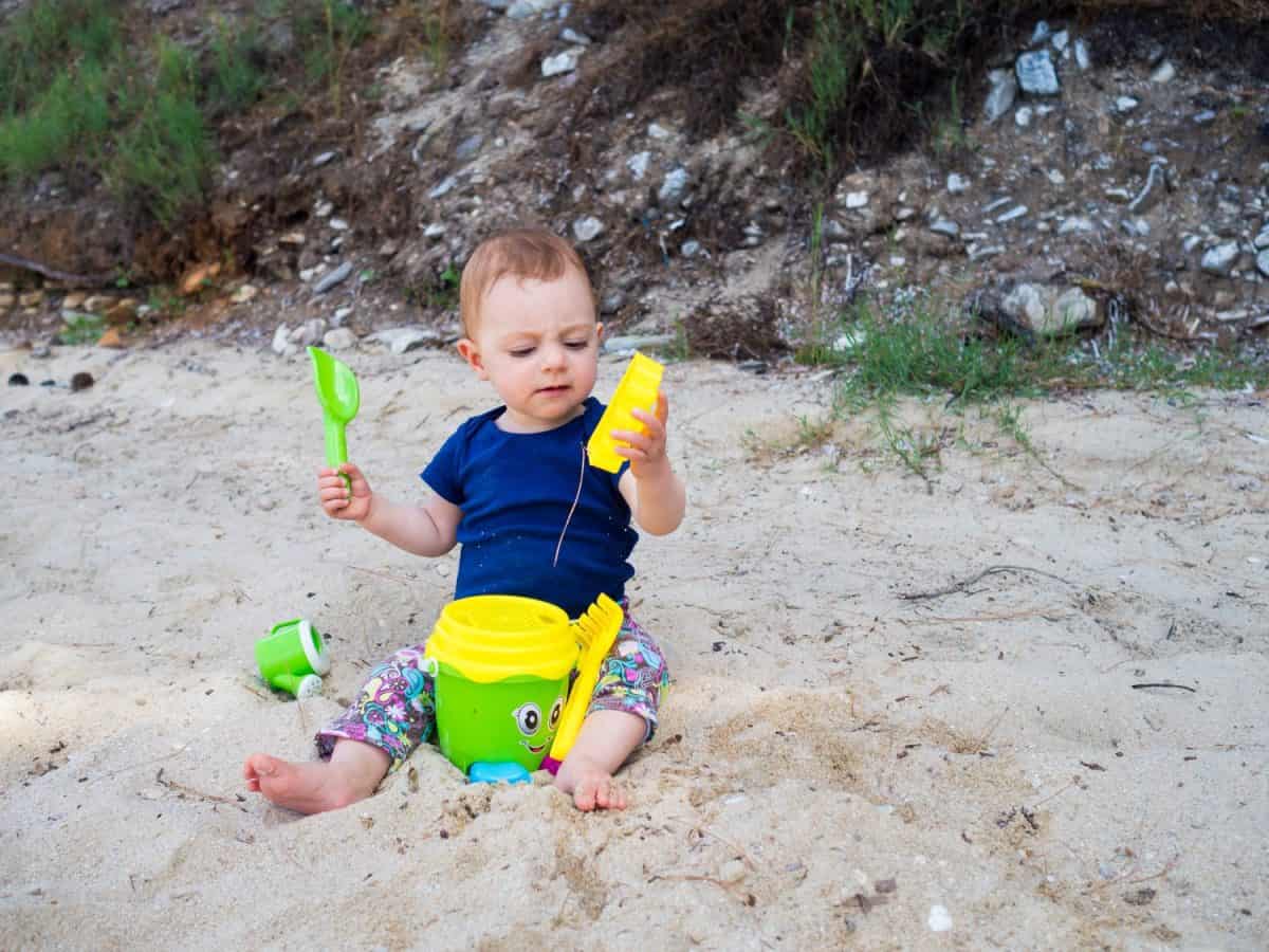 Little baby girl having some fun with her toys on a sandy beach of the Greek island of Thasos, Aegean sea.