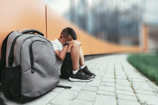 child with backpack in depression is sitting on the floor doesn't want back to school