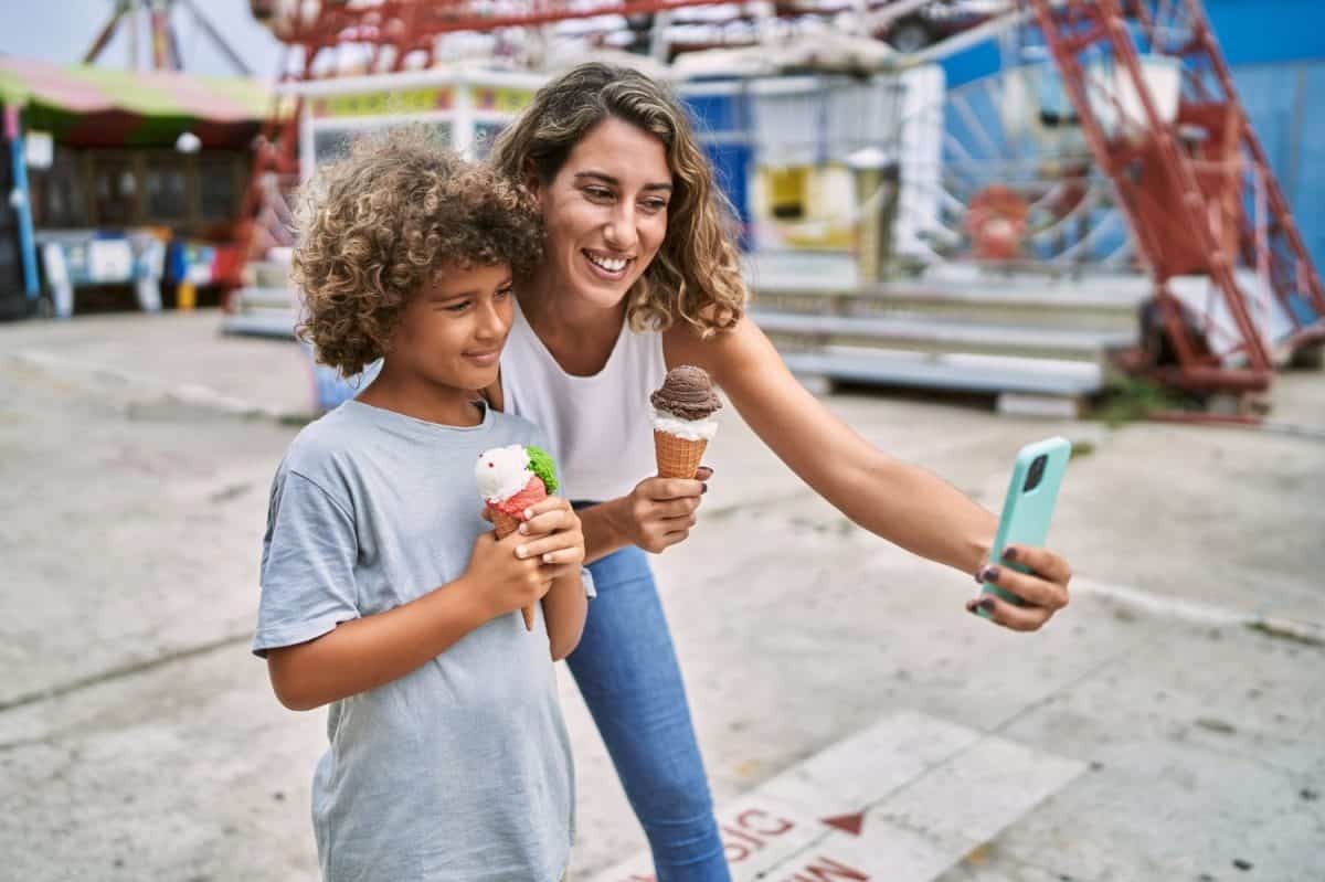 Mother and son eating ice cream make selfie by the smartphone at theme park