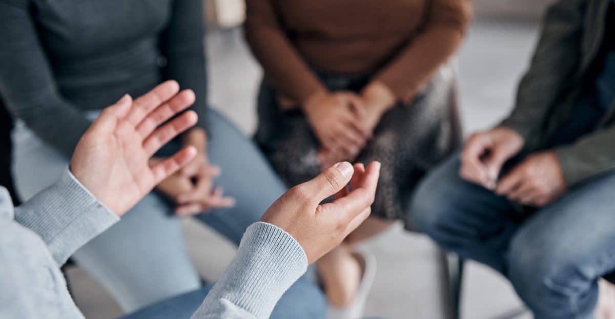 Support with group, therapy and mental health with hands and help, people together talking about problem and crisis. Psychology, healthcare and trust, respect and community in counseling for trauma