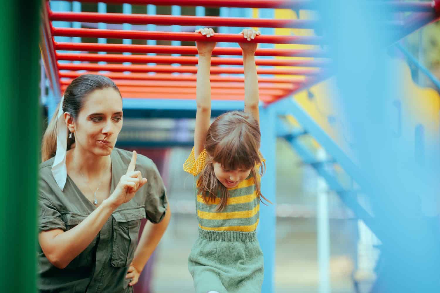 Mom Forbidding her Child to Climb on a Dangerous Playground Equipment. Caregiver babysitting applying strict safety rules for the little kid