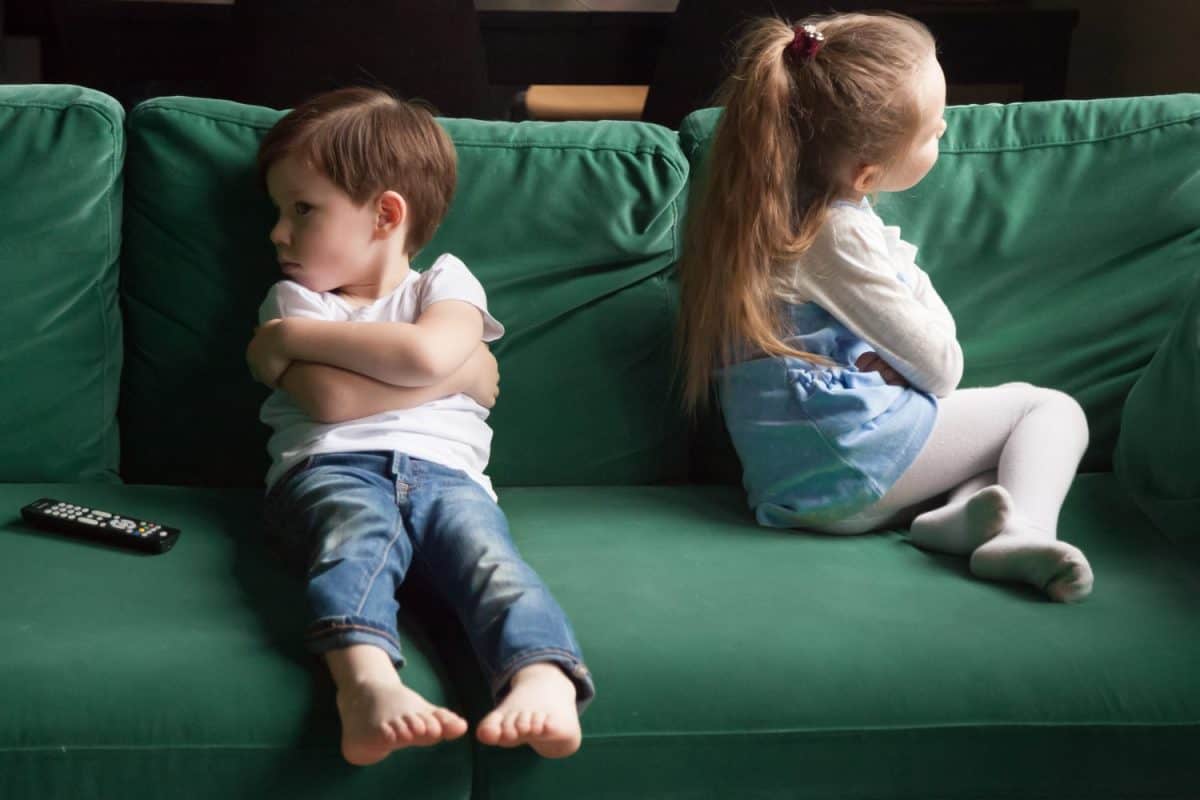 Upset siblings boy and girl sulking sitting with arms crossed on sofa not talking, kids brother sister ignoring each other after fight about tv channel choice, children conflicts and rivalry concept