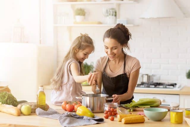 Mother and daughter preparing tasty food at kitchen. Mommy teaching lovely kid to cook. Happy smiling mom and loving child spending time together at home. Healthy meal and dinner preparation