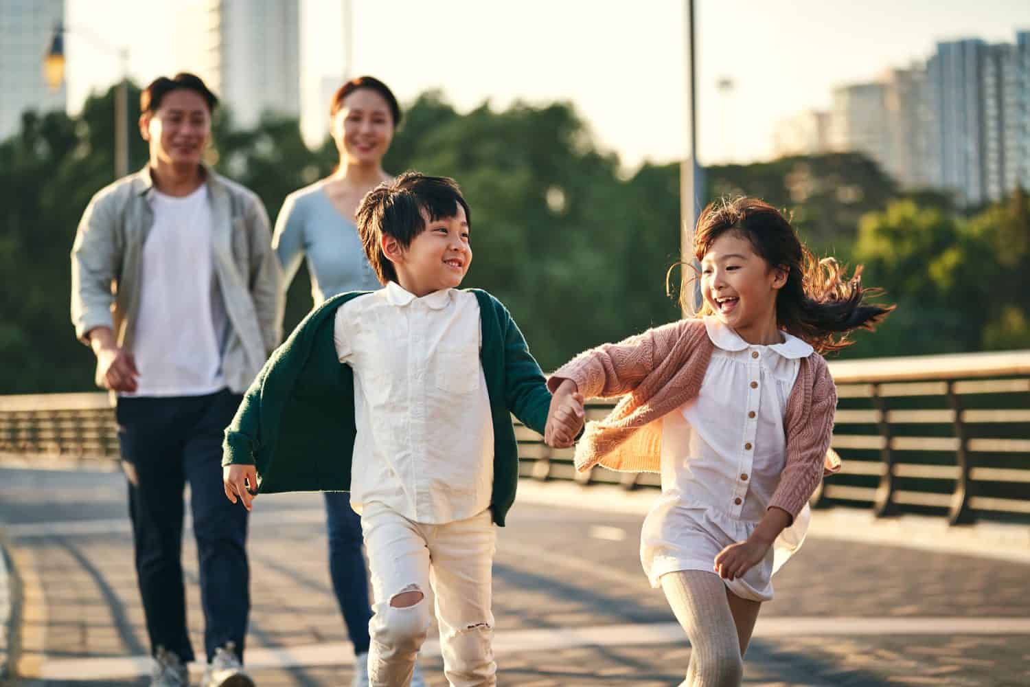 happy asian family with two children walking on pedestrian bridge in city park