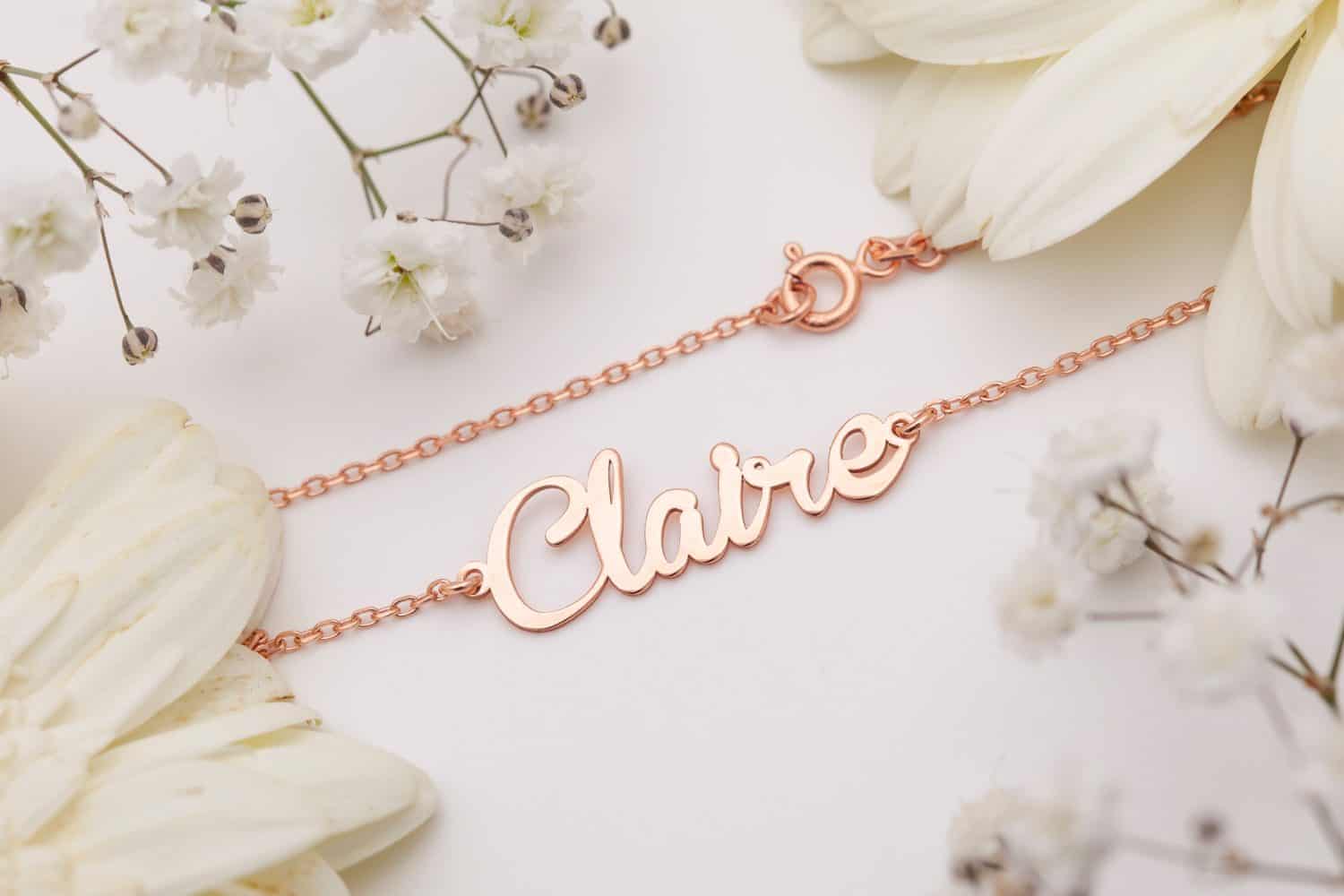 Gold necklace with name inscription displayed on a floral background. Jewelry photo for e-commerce, online sale, social media.