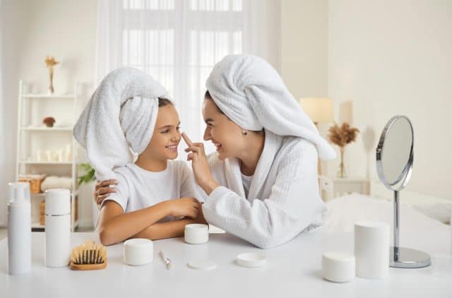 Mother and child having fun during skin care routine. Happy beautiful mommy and pretty little daughter sitting at beauty table, enjoying self care, applying face cream and having good time together