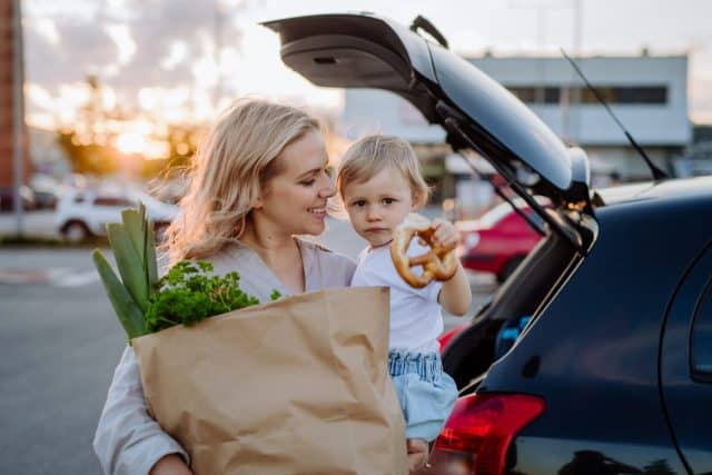 Young mother with little daughter after shopping holding zero waste shopping bags with grocery near car.