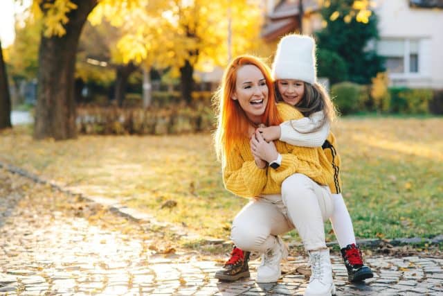 Happy mother and daughter walking in the autumn park. Woman and child daughter playing outdoors. Mom and girl laughing outdoors. Autumn fashion. Happy family having fun together.
