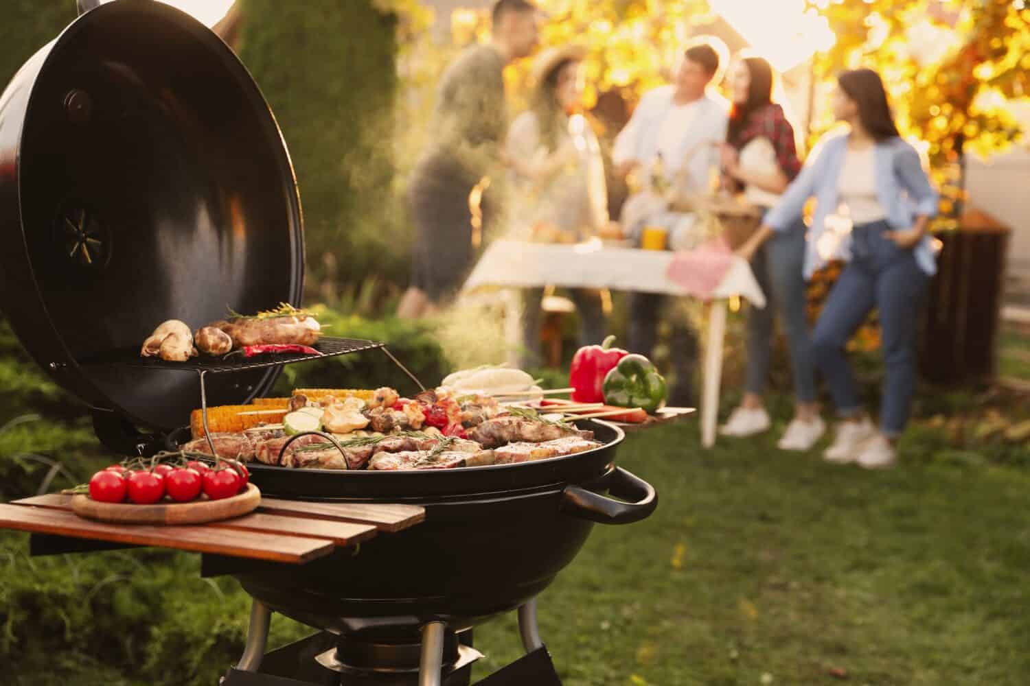 Group of friends having party outdoors. Focus on barbecue grill with food. Space for text