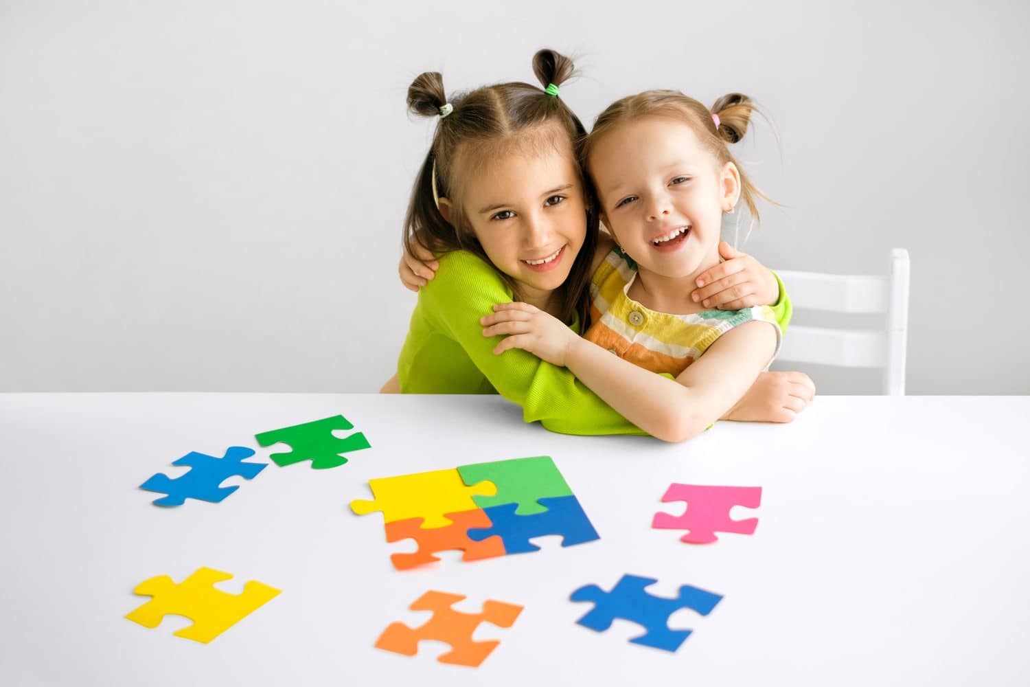 Charming nice girls hugging at the table. Children are happy to engage in a joint hobby together. multi-colored puzzle pieces are a symbol of awareness about autism