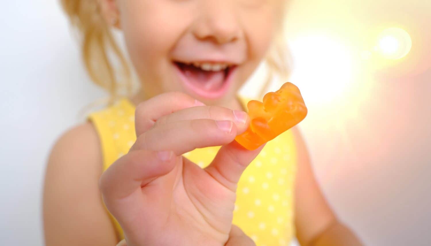 cheerful small child holds candy, blonde girl 3 years old wants eat gelatinous sweets with smile, gummy bear, kid has good appetite, happy childhood, balanced diet, sweet life, unhealthy food, halal