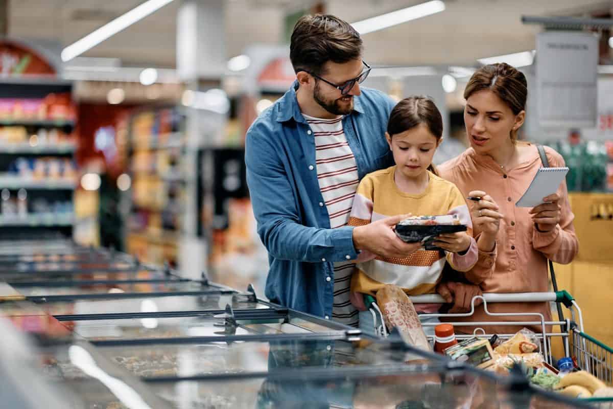 Little girl and her parents choosing groceries while shopping at supermarket. Copy space.