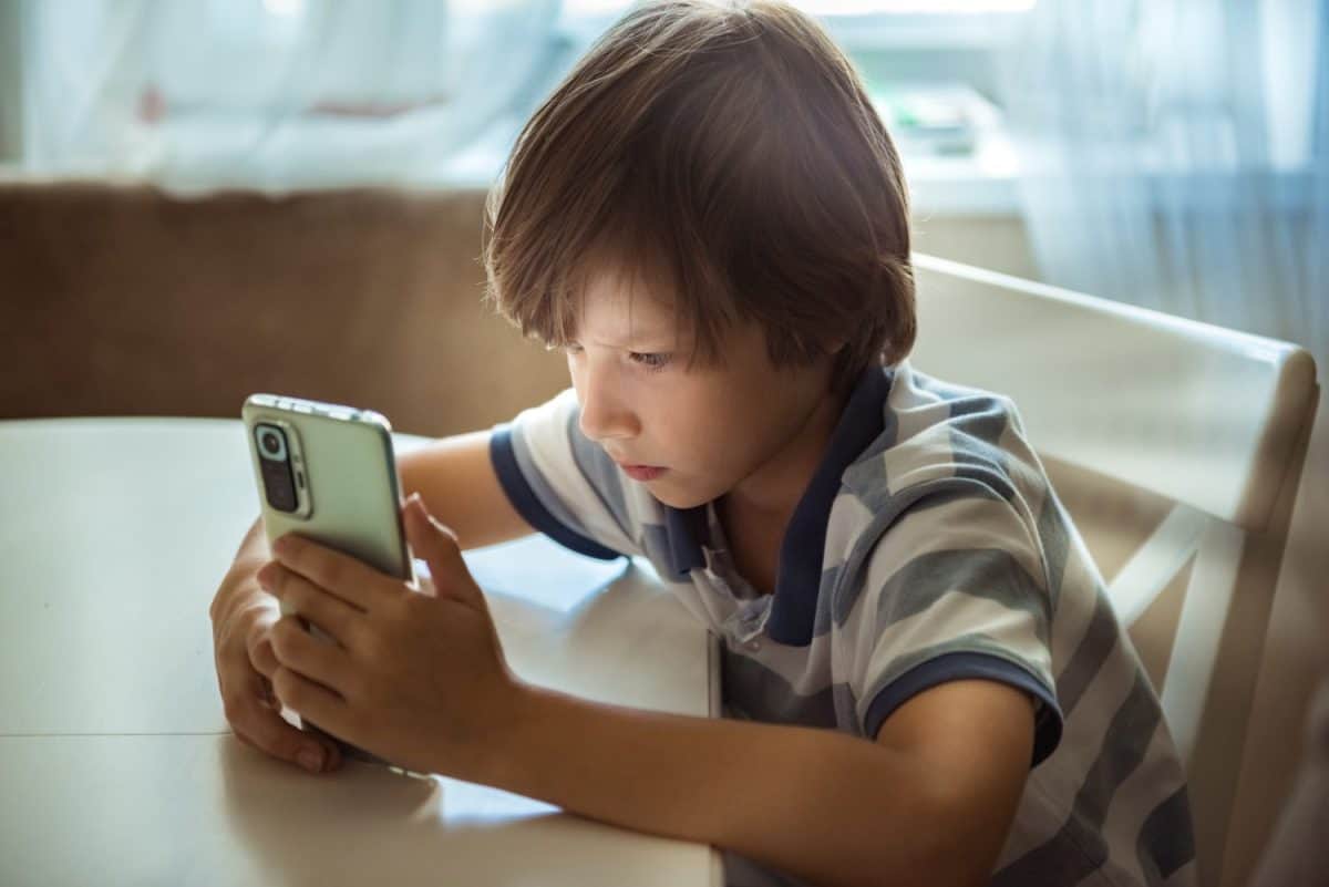 Cute child using smart phones, playing games. Children's screen addiction and parent control concept. Sensitive content on screen