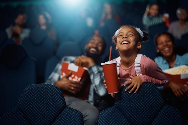Happy African American girl enjoying during movie projection in cinema.