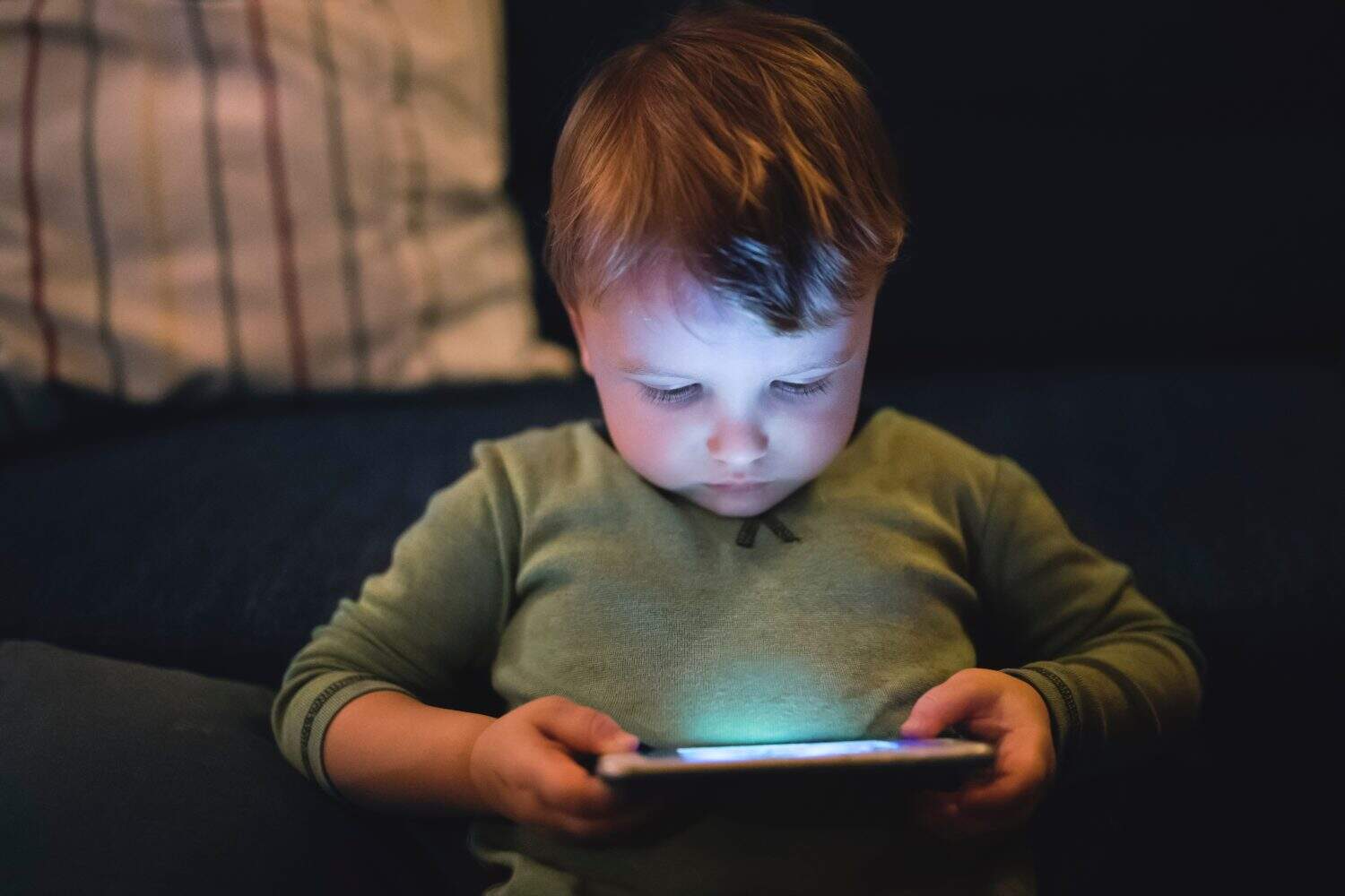 Cute boy sitting on bed watching something on smartphone. Children's screen time.