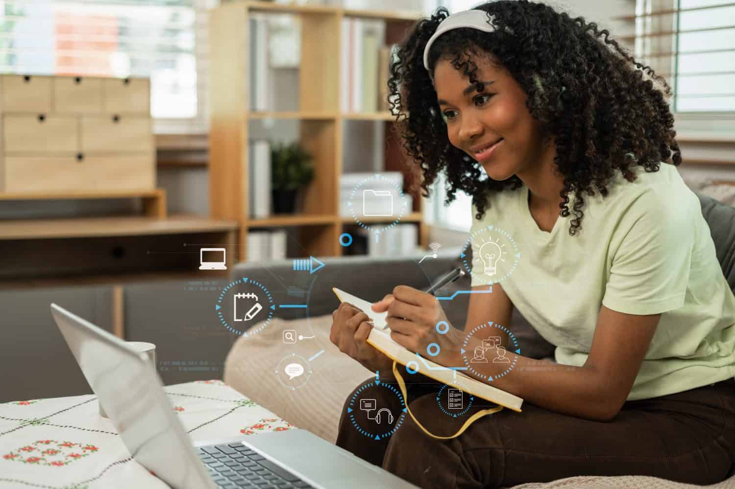 Smiling woman in headphones taking notes, motivated interested student studying online, using tablet and laptop, watching webinar training or listening to lecture, remote education concept.