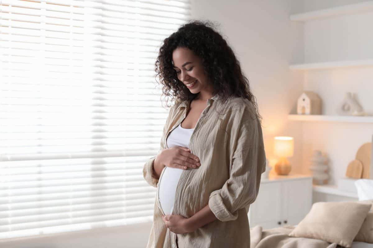Portrait of beautiful pregnant woman near window at home, space for text