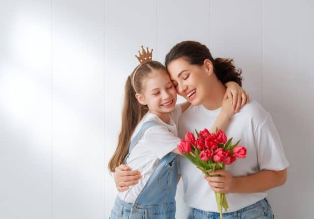 Happy women's day. Child daughter is congratulating mom and giving her flowers. Mum and girl smiling and hugging. Family holiday and togetherness.