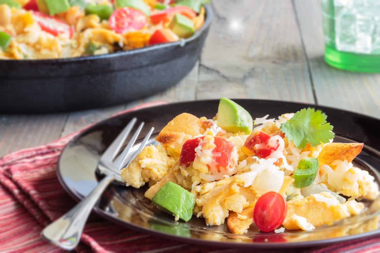 Tex-Mex breakfast migas made of eggs scrambled with onions, red bell pepper, jalapeno, cheese, topped with cherry tomatoes, avocado and cilantro