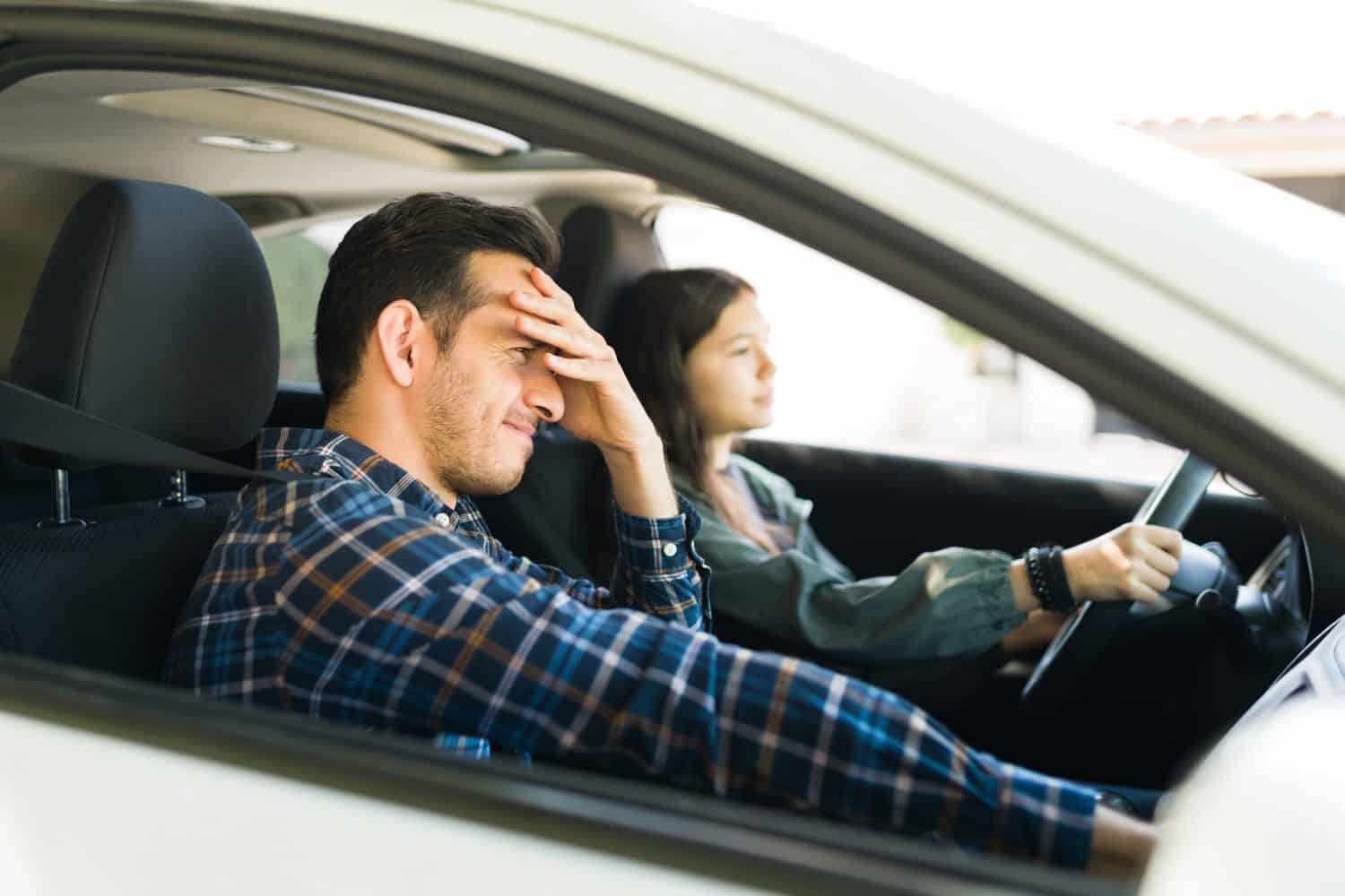 Teen daughter driving his dad's car above the speed limit during her driving lessons next to her upset looking father