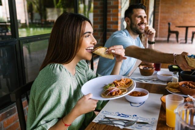 young latin woman eating mexican tacos on a restaurant terrace in Mexico Latin America, feeling happy on a summer day
