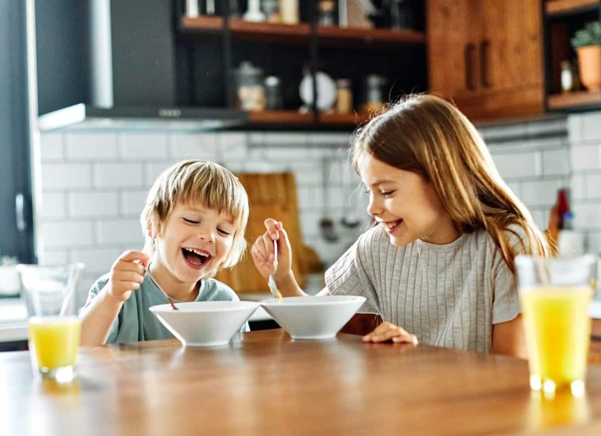 Portret of brother and sister having fun together eating breakfast in kitchen