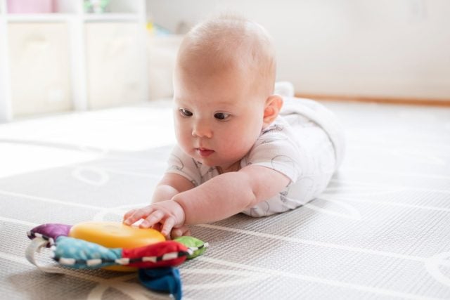Little baby girl is playing with a toy during tummy time. Baby reaching for a musical toy. Baby development