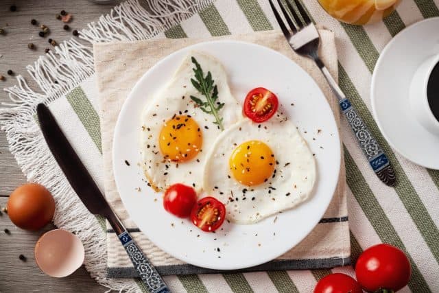 Fried eggs for breakfast. Healthy breakfast with vegetables and herbs. Fried eggs on a white plate. Serving on the table. Morning fried eggs with coffee and orange juice.