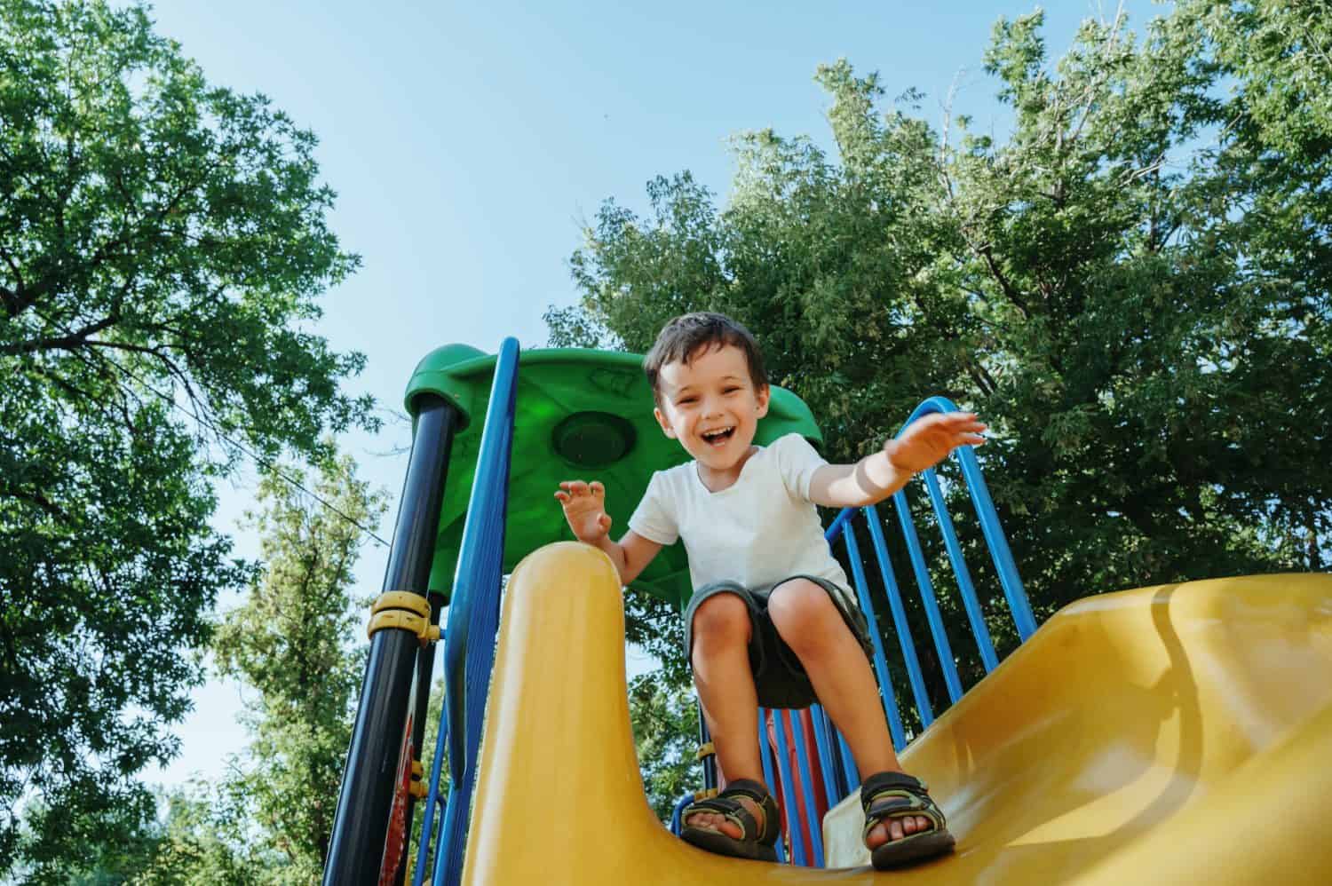 happy preschooler boy playing on a slide on the playground in summer