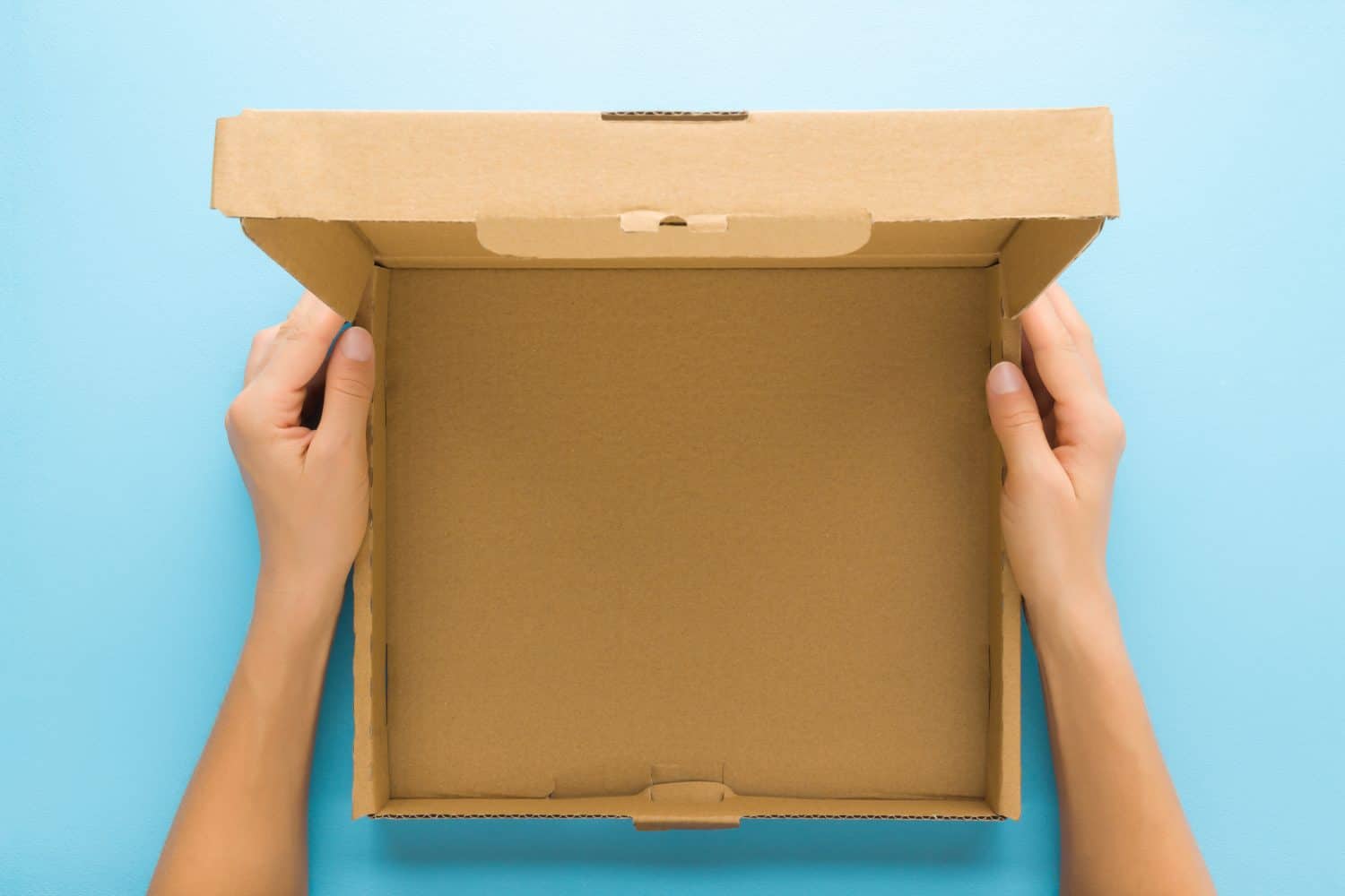 Woman hands holding opened brown carton box on light blue table background. Pastel color. Closeup. Empty place for different things, goods, food or products packaging for delivery. Point of view shot.