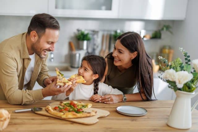 Mom, dad and daughter are eating together at home. Happy family eating pizza at home.