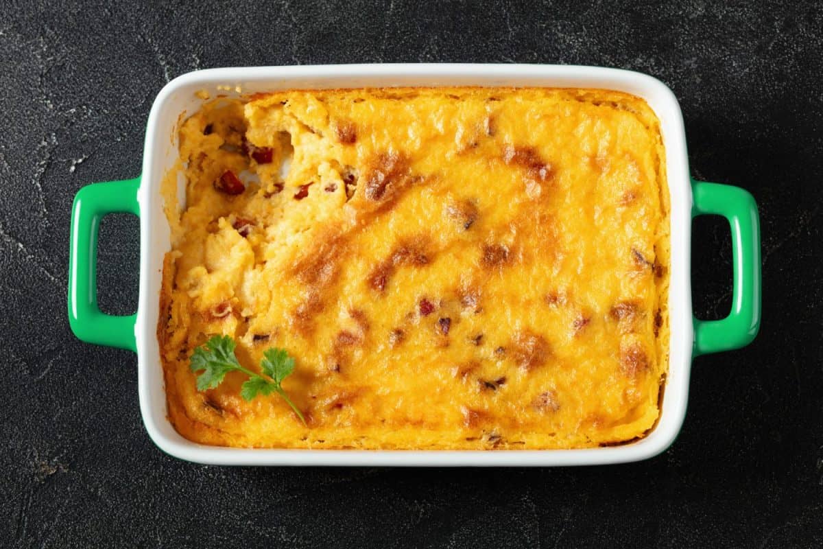 cheesy smoked sausage grits casserole in green baking dish on dark concrete table, horizontal view from above, flat lay, close-up