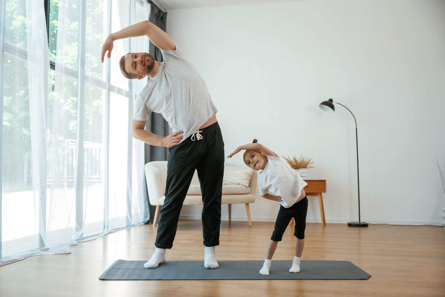 Spine exercise. Father with little daughter are doing yoga at home.