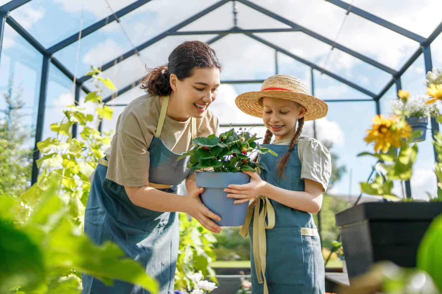 Happy mother and daughter are gardening in the greenhouse. Child is helping her mom and learning about botany.
