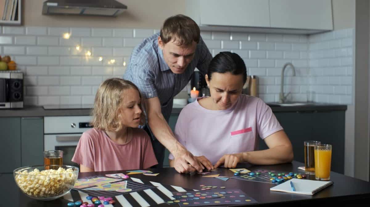 Family of three playing board games at a table in their kitchen, connecting the geometric shapes of a tangram puzzle. Family lifestyle concept